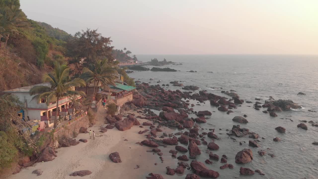 costa rocosa del océano y edificios antiguos en la playa de arambol al atardecer en goa, india - tiro aéreo
