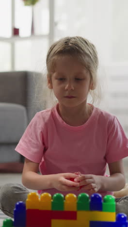 focused girl builds wall taking multi-colored plastic blocks while brother playing with vehicle toys. children enjoy fun activity at home closeup