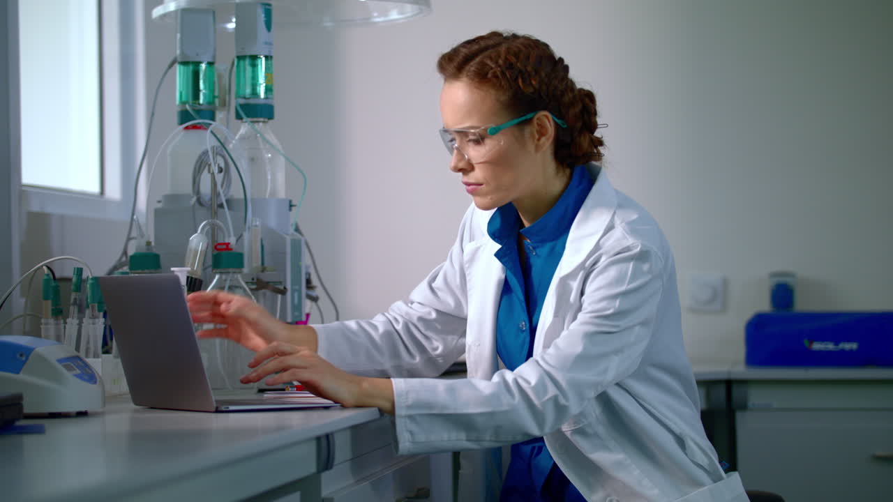 Female scientist working in laboratory. Lab worker typing report on computer