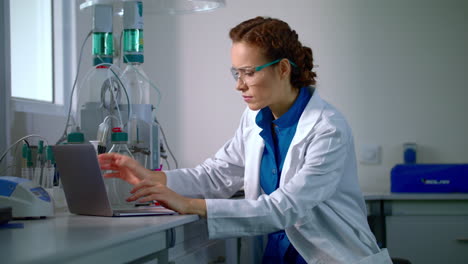 female scientist working in laboratory. lab worker typing report on computer