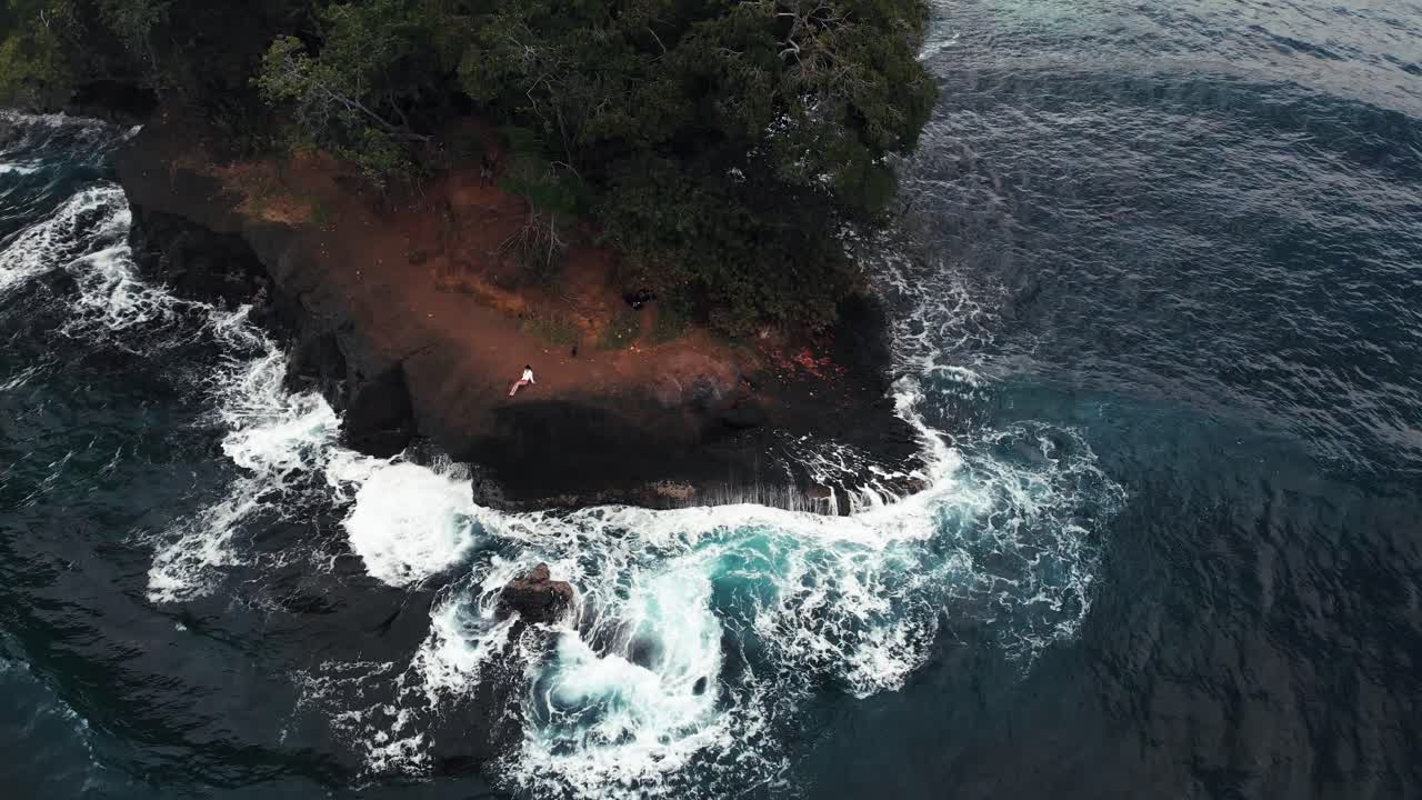 A Sexy Lady Posing On The Rocky Island With Lush Trees In Costa Rica With Ocean Waves Splashing At The Bottom - Aerial Shot