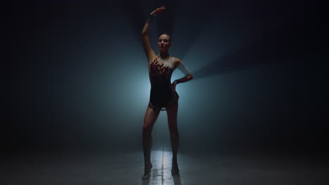 Gymnast-girl-standing-with-raised-hand-dark-space.-Sportswoman-posing-indoors.