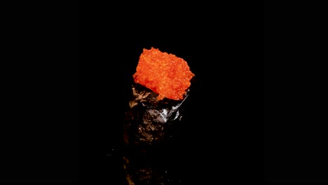 a single piece of gunkan maki sushi topped with bright orange fish roe rotates smoothly against a seamless black background under dramatic studio lighting