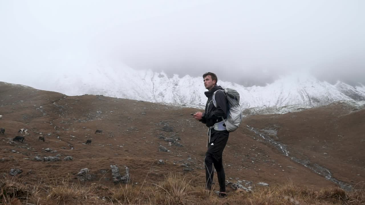 Slow motion shot of hiker in foggy and rainy mountain environment looking on phone and navigating his way