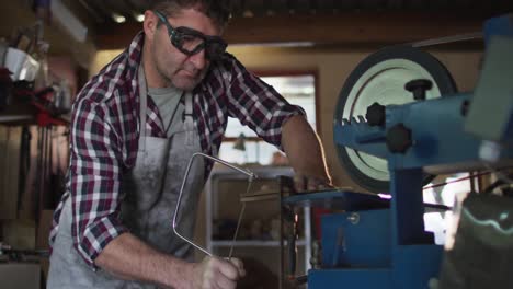 caucasian male knife maker in workshop wearing glasses and using saw