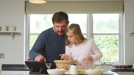 Padre-E-Hija-En-Pijama-Horneando-En-La-Cocina-De-Casa-Siguiendo-La-Receta-En-Una-Tableta-Digital