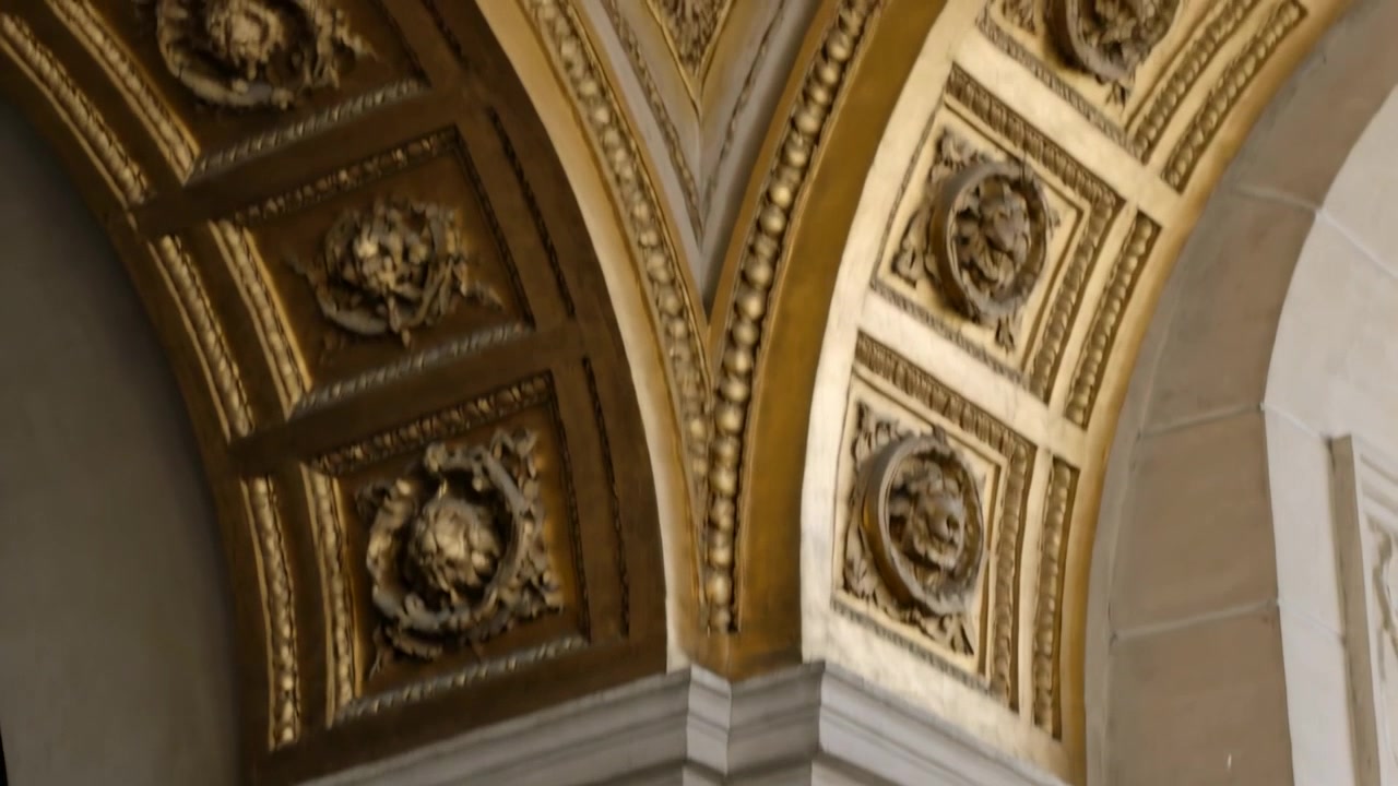 Câmera panorâmica recuando e inclinando para cima em hall de escada, mostrando corrimão, pilastras, pilar e painéis dourados.