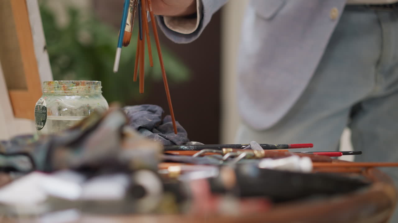 아티스트가 스튜디오 클로즈업에서 을 모으고, 회색 의상을 입은 남자가 그림을 그리는 장비를 정리하고, 가게에서 작업을 마무리합니다.