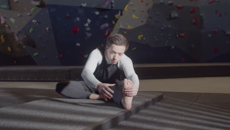 joven deportista enfocado haciendo ejercicios de calentamiento y estirando las piernas en un gimnasio de boulder 2