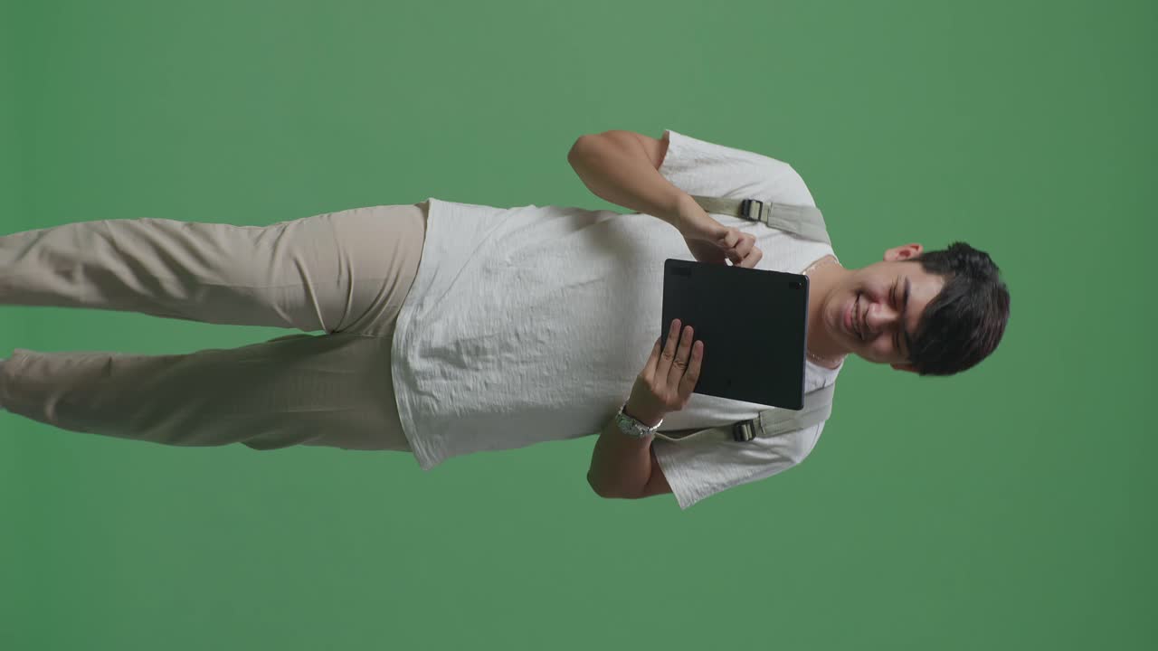 estudiante hombre asiático usando tableta y caminando en el estudio de pantalla verde