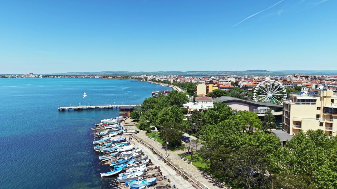 Vista de barcos atracados na costa com um cenário de cidade ao longe sob um céu azul claro durante o dia.