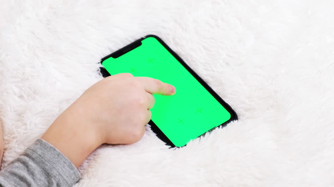 가을 가진 유치원 아이는 집에서 휴대 전화에서 사진을 가진 페이지를 뒤집습니다. 아이는 스마트폰 녹색 화면을 사용하고 손에 들고 있습니다. 기술 생성. chromakey에 초점을 맞추십시오.