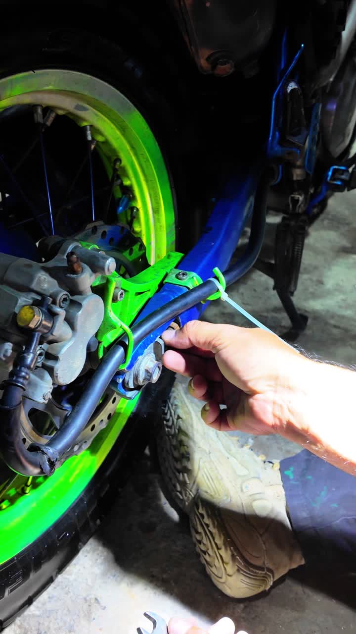 A person adjusting the motorcycle rear chain tensioner with their hands in a garage setting