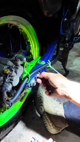 a person adjusting the motorcycle rear chain tensioner with their hands in a garage setting