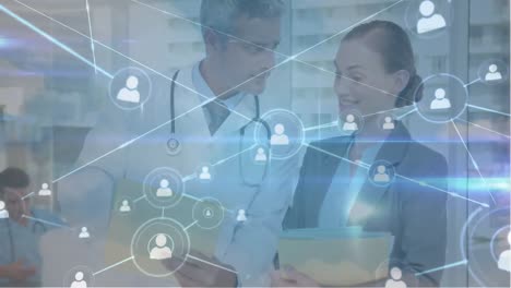 Animation-of-connected-people-icons-over-caucasian-doctors-discussing-medical-report-in-hospital