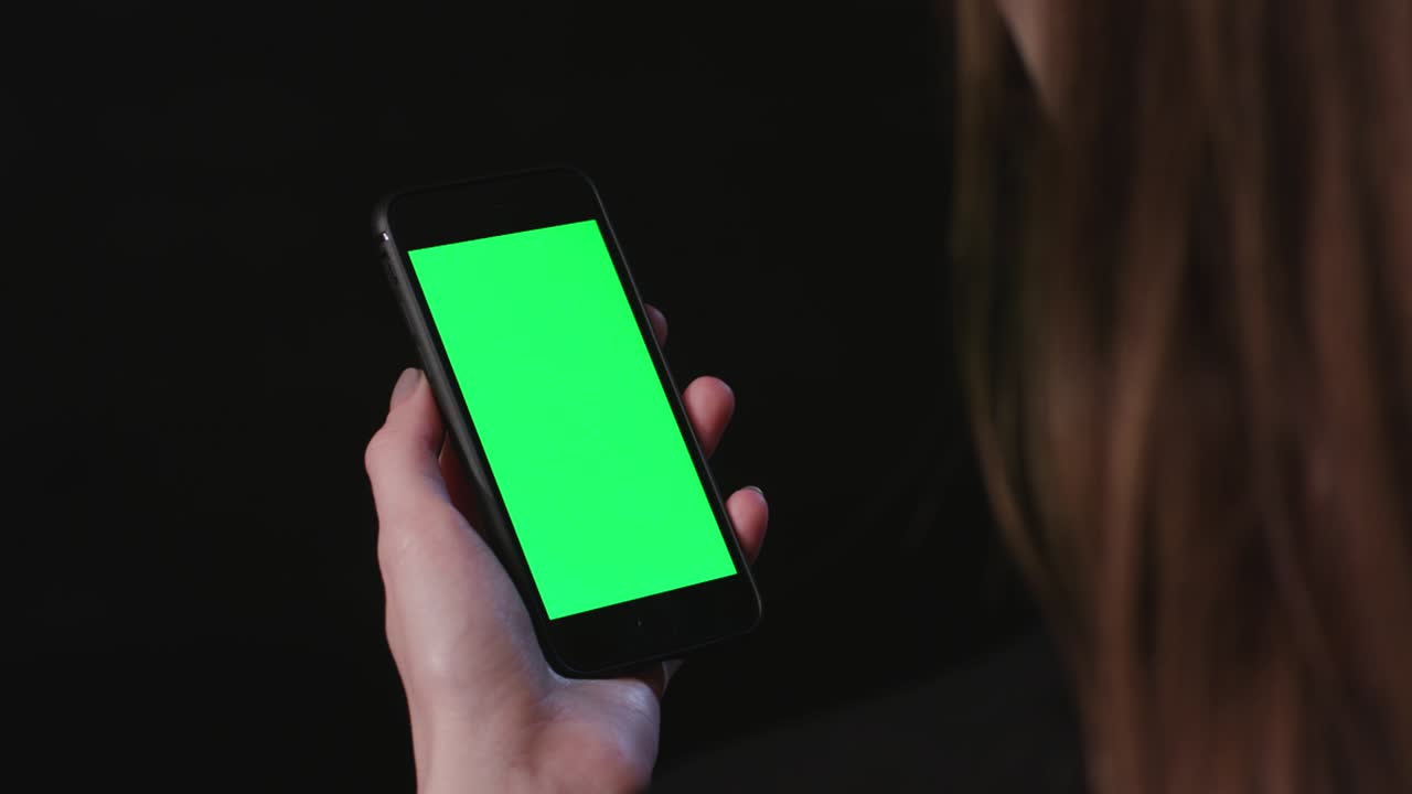 여성은 초록색 스크린 스크롤로 전화를 들고 있습니다.