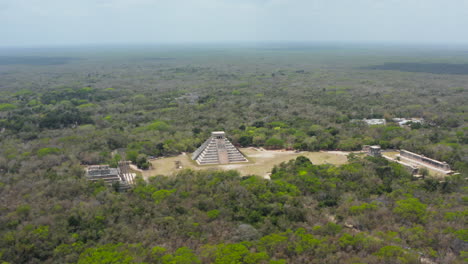 Drone-Descendiendo-Y-Orbitando-Alrededor-De-Un-Asentamiento-Histórico.-Vista-Aérea-De-Puntos-De-Referencia-Y-Vasto-Bosque.-Monumentos-Historicos-De-La-Epoca-Precolombina,-Chichen-Itza,-Mexico.