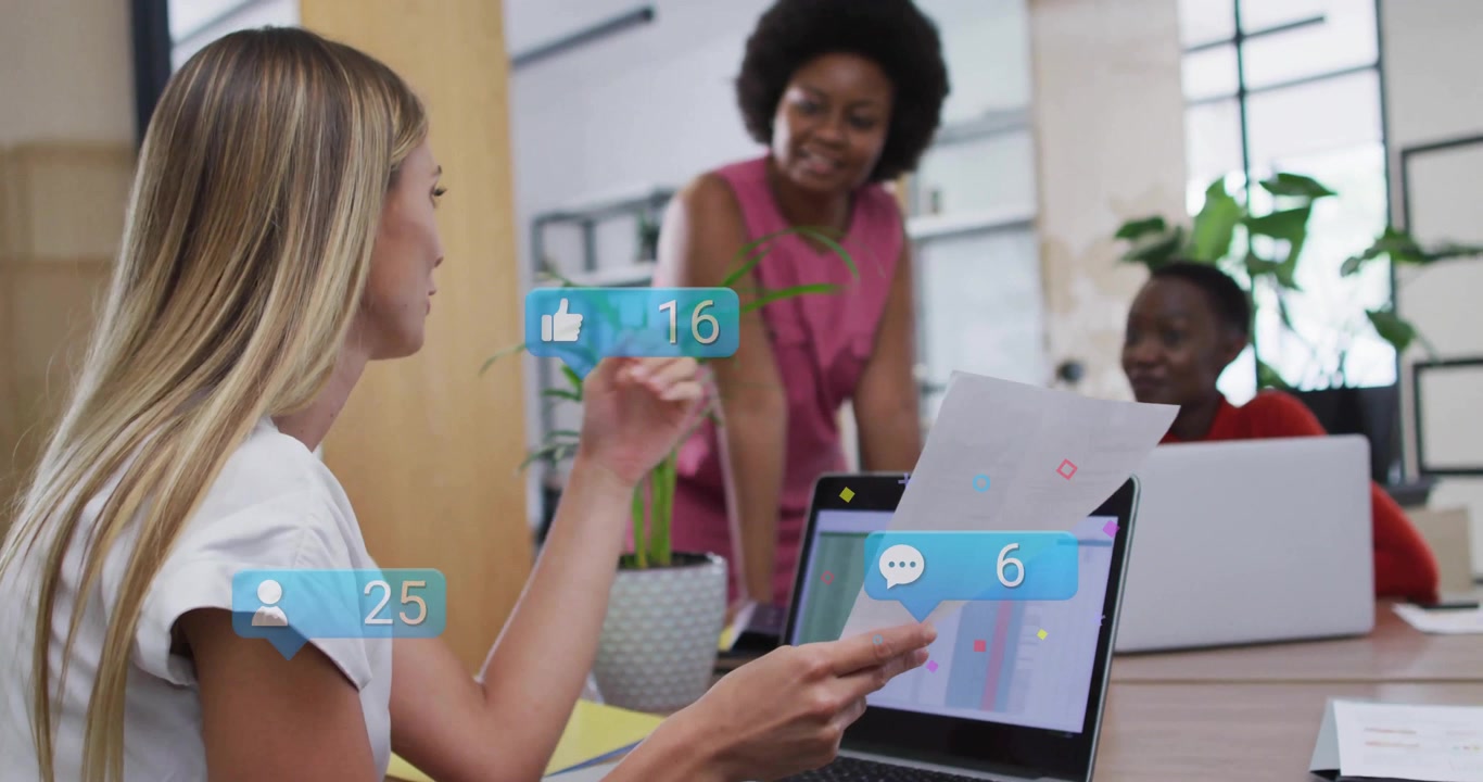 Collega bionda che prende un rapporto e indica i dati su un portatile in ufficio, con icone social animate che variano