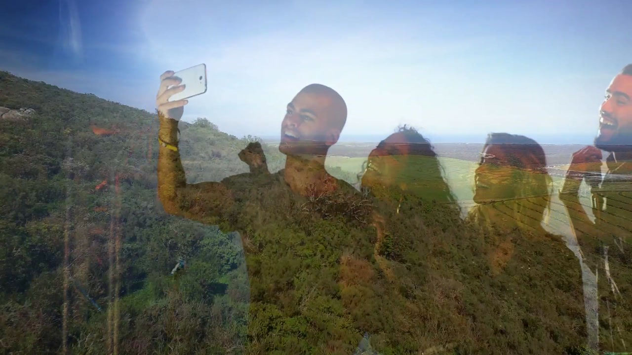 Center man raising white phone for travel selfie, group leaning reviewing photos with faint overlay