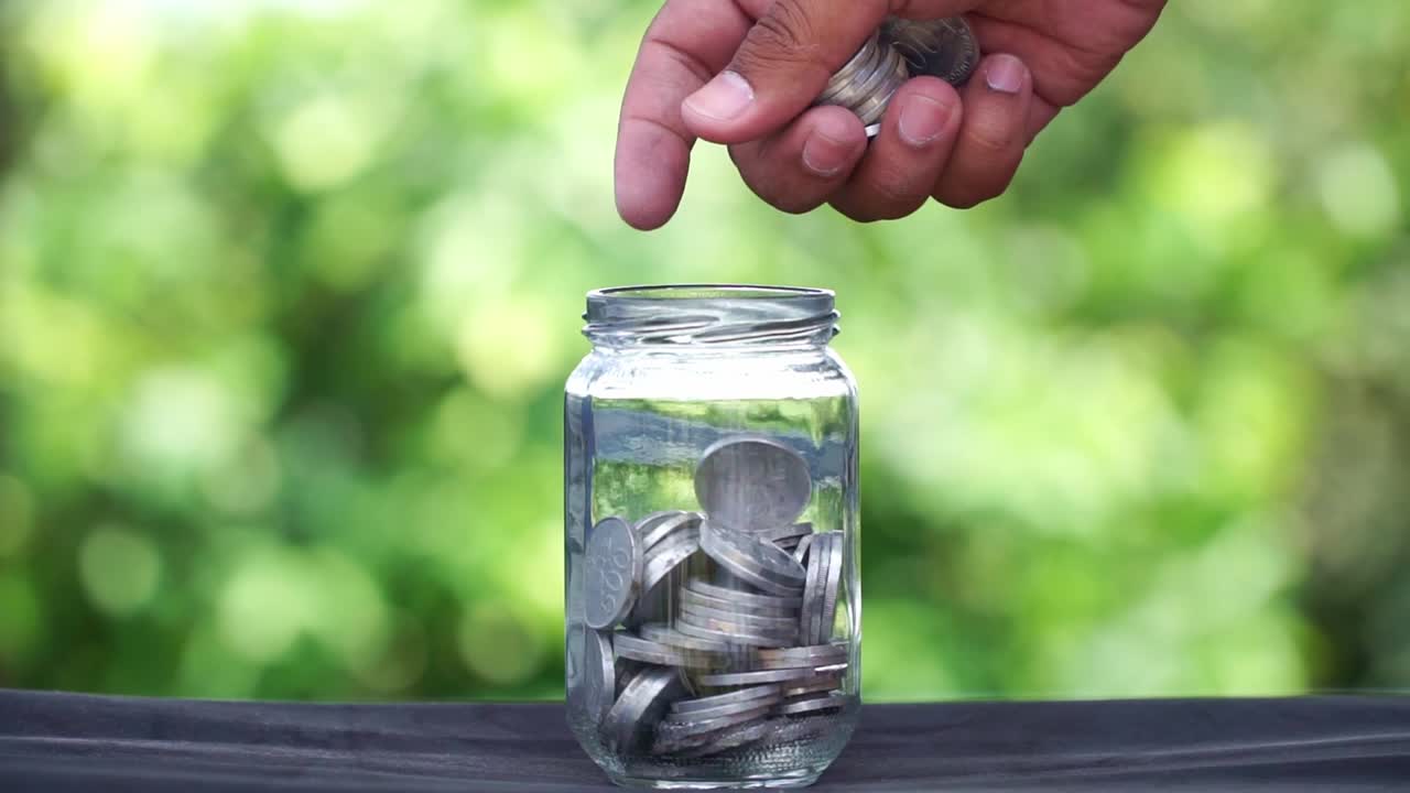 Hand holding coins and putting them into a glass container. Business concept, profit and saving.