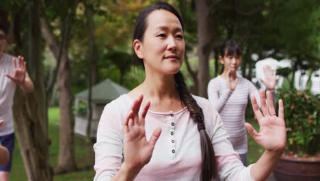 Happy-asian-parents-exercising-in-garden-with-son-and-daughter,-practicing-tai-chi-together