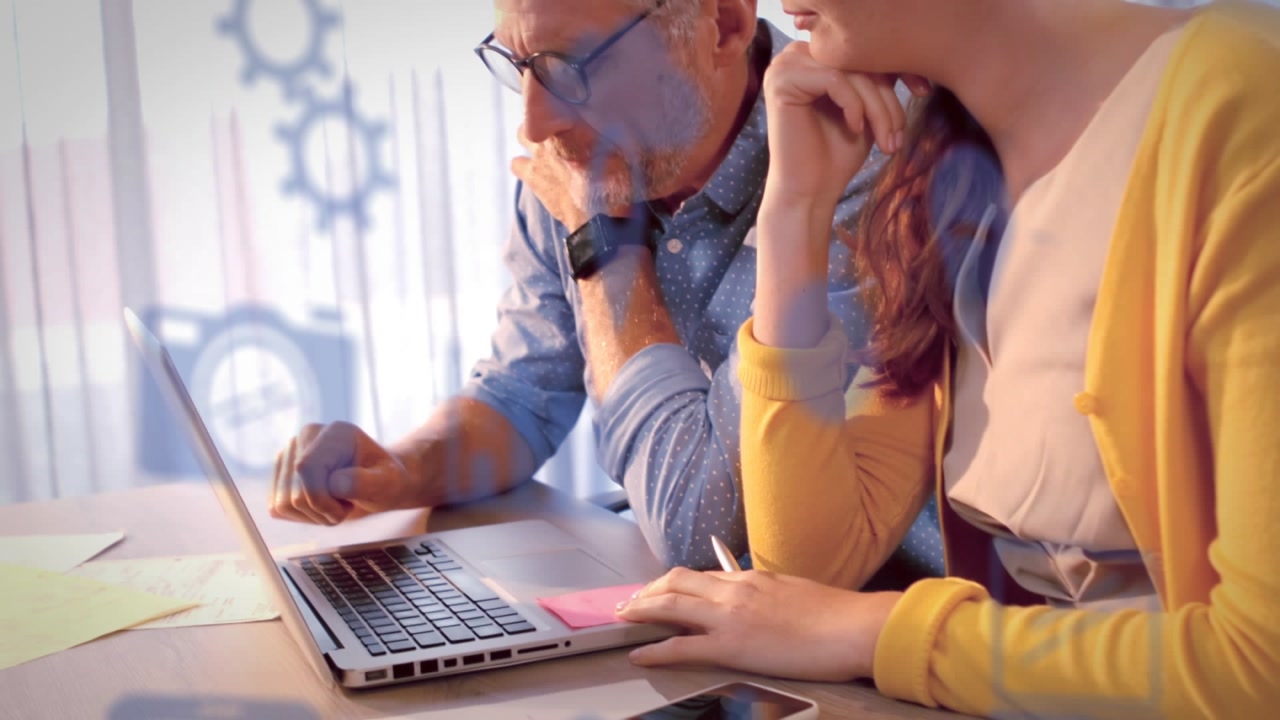 In the image, we see two businesspeople discussing over a laptop in an office