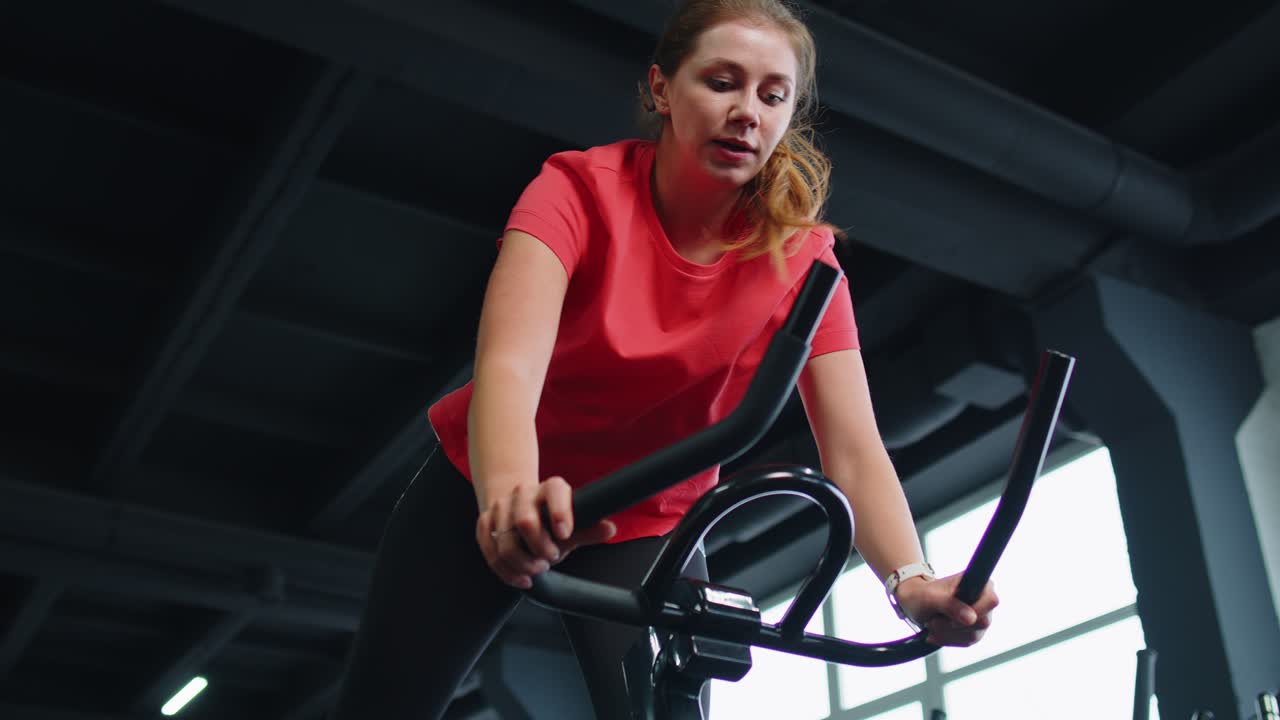 Athletic girl performing jumping aerobic riding training exercises on cycling stationary bike in gym