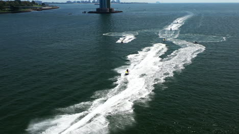 aerial-pull-away-and-orbit-above-a-group-of-jet-ski-riders-on-the-waters-between-Brooklyn---Staten-Island,-New-York,-with-the-Verrazano-Bridge-in-the-background
