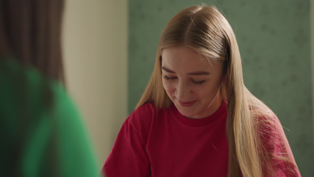 Кавказская девушка с улыбкой демонстрирует готовое вязаное изделие в уютной комнате, держит небольшую вещь ручной работы, чтобы показать ее другу, радостное выражение лица, видна красная пряжа и аккуратные стежки, праздничная демонстрация поделки