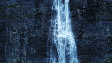 tilt up shot showing waterfall falling in front of steep mountain wall during dusk - slow motion shot
