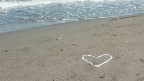 bubbly wave washes over stone pebble heart in sand