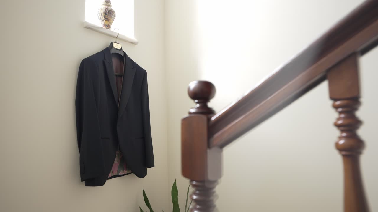 black suit jacket on a hanger near a wooden staircase in a bright, minimalist hallway