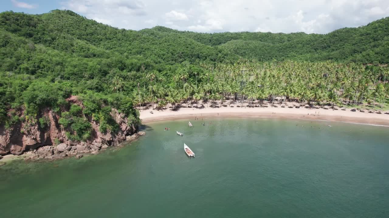 Aerial drone shot of a pristine tropical bay with lush palm trees, serene turquoise water, and people enjoying a calm summer day