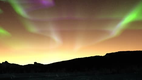 dark mountain peaks at night with purpel green auroras in the sky