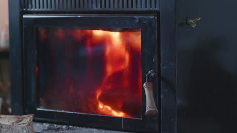 fuego caliente y rugiente detrás de la puerta de cristal negra y llena de hollín de la chimenea interior