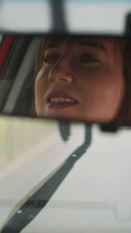 reflejo de una mujer sonriendo en el espejo trasero contra limpiadores limpiando el parabrisas de las gotas de lluvia. una mujer conductor disfruta de un viaje en un día de lluvia de primer plano en cámara lenta