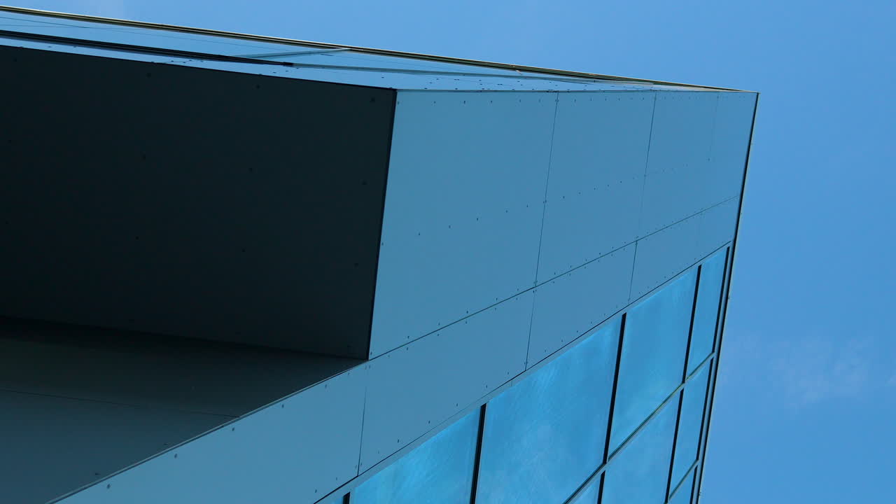 esquina de un edificio moderno con paneles elegantes y vidrio azul reflectante contra un cielo despejado