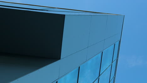 esquina de un edificio moderno con paneles elegantes y vidrio azul reflectante contra un cielo despejado