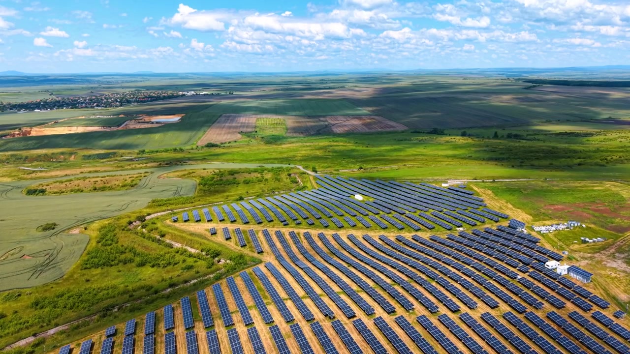 Solkraftværk med rækker af fotovoltaiske paneler på bakker. Luftfoto med vidvinkel af alternativ energistation på grønne marker under blå himmel med skyer.