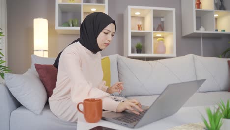 Mujer-Con-Pañuelo-En-La-Cabeza-Mirando-Una-Computadora-Portátil-En-Casa-Y-Escribiendo.