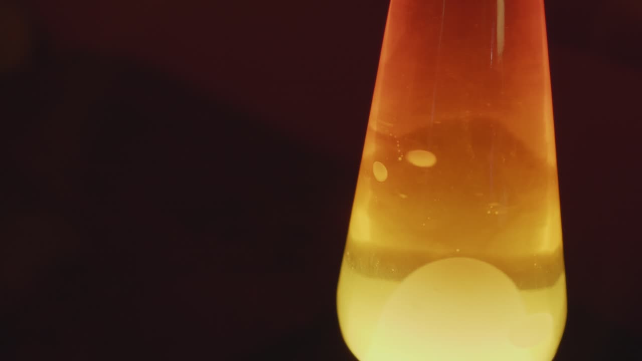 Close up of a vintage lava lamp in a warm and vintage setting. Orange lighting and bubbles create a retro atmosphere. Shot in 60 Frames for slow motion
