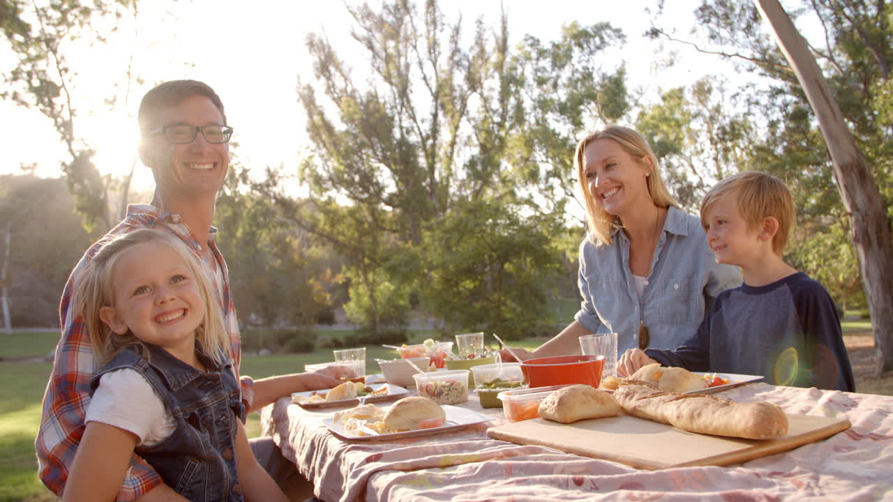 familia joven en un picnic en una mesa en un parque mira a la cámara