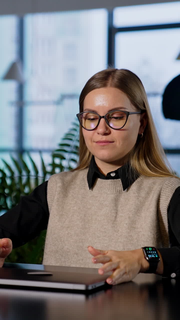Confident blonde woman puts on glasses. Lady opens laptop in front of her on the table and starts work. Vertical video