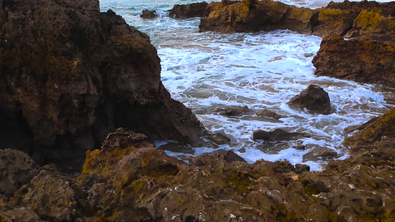 Ripresa al rallentatore di onde marine spumeggianti turchesi e bianche che si infrangono su rocce marroni aguzze lungo la costa rocciosa portoghese alla luce del giorno