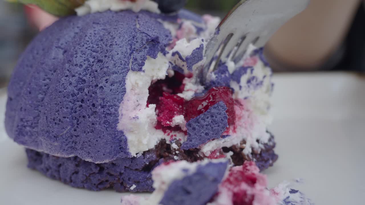 Close-up of a partially eaten purple cake with fruit and cream filling