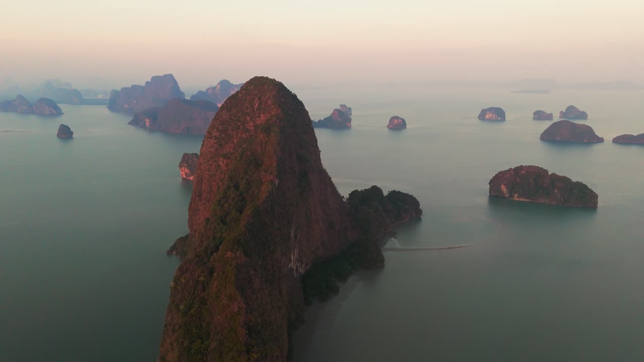 Phang Nga Bay with towering lush vegetated limestone karsts rising from the calm waters, aerial pullback at sunrise