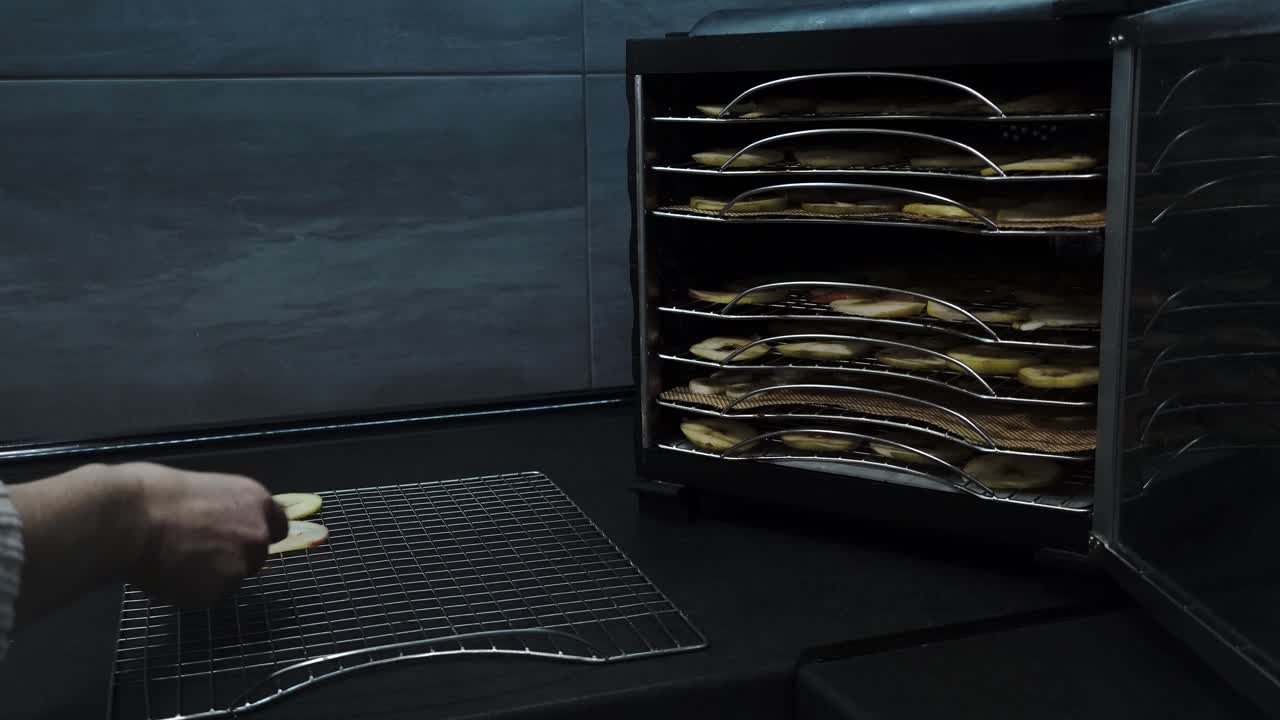 deshidratador de frutas en el hogar: preparando manzanas secas en la cocina, la mujer arregla manzanas en rodajas en una bandeja de metal