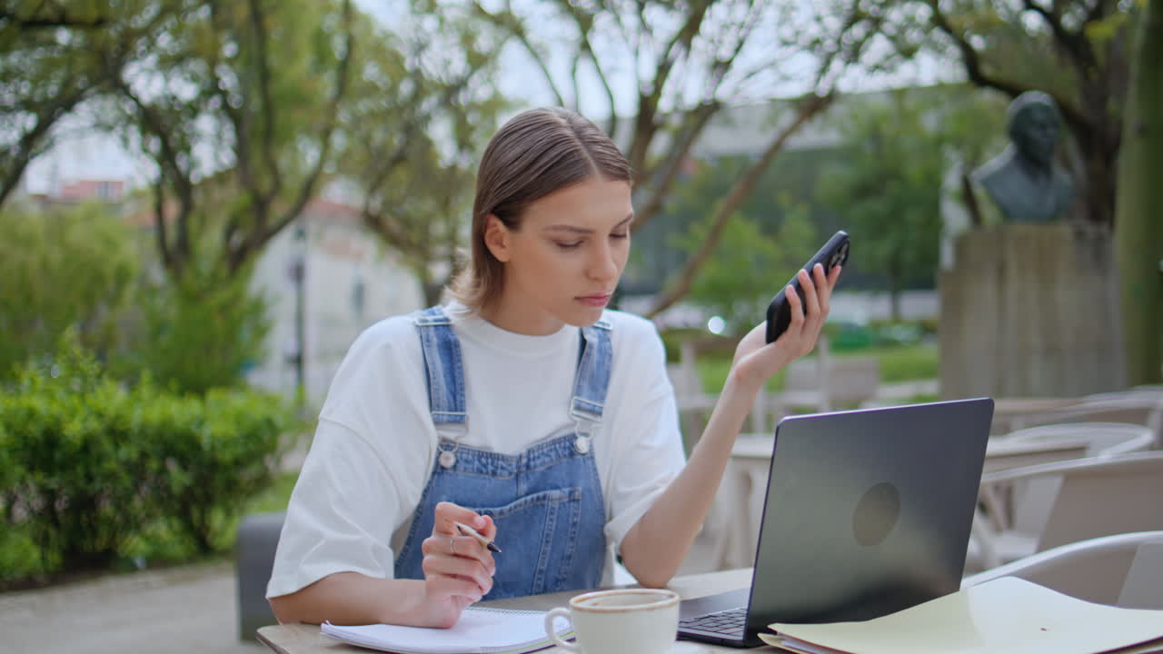 Serious freelancer making notes in notebook at outdoors cafeteria closeup