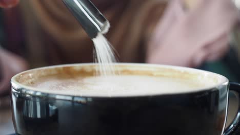 close-up of a person adding sugar to a cup of cappuccino