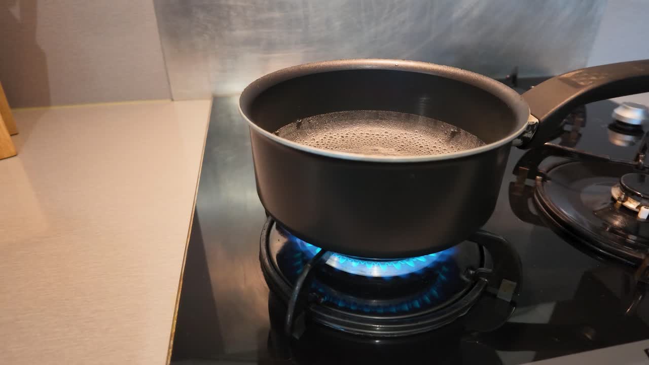 Primo piano dell'acqua che bolle in una pentola nera su una fiamma blu di un fornello a gas